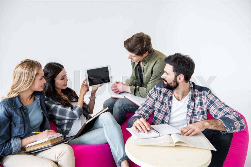 Students sitting on beanbag chairs and studying with digital tablet in studio on white , stock photo