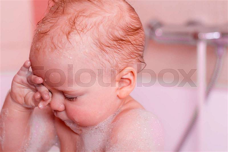 Baby boy rubbing eyes in bath tub. Infant kid in a foam. Close-up portrait, stock photo