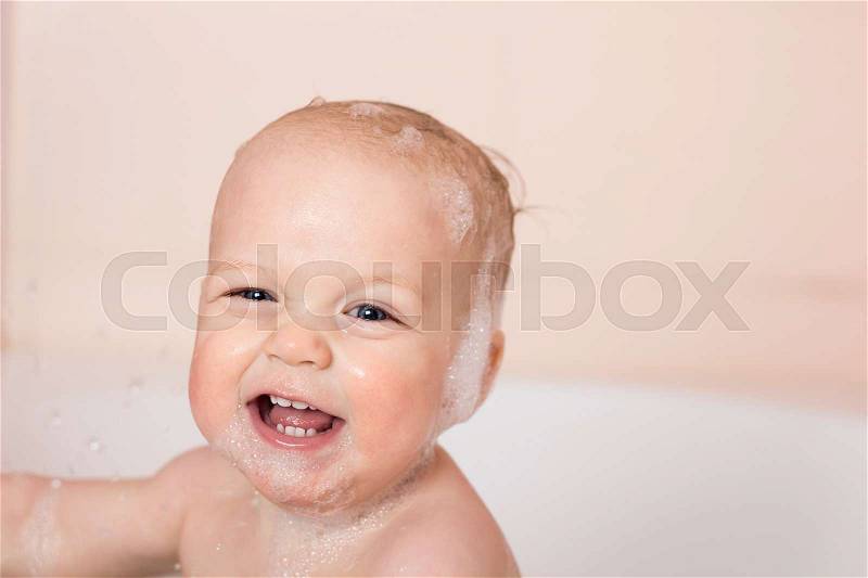Cute smiling baby boy in a tub. Funny infant kid laughes and looking at camera, stock photo