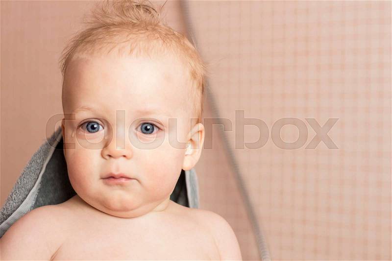 Awesome infant boy after shower. Cute blue-big-eyed baby boy in a towel looking at camera, stock photo