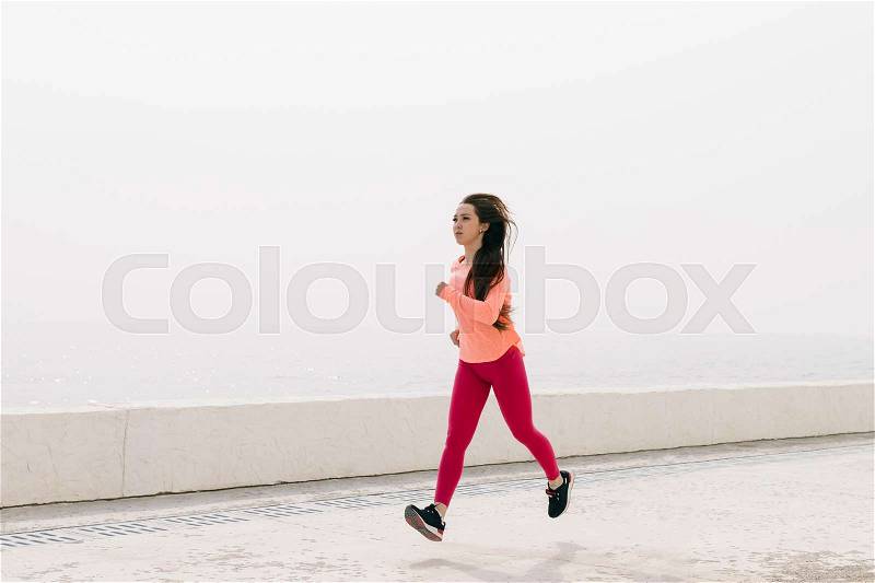Slim girl in red sportswear running on the beach in the morning, wide angle shooting, stock photo