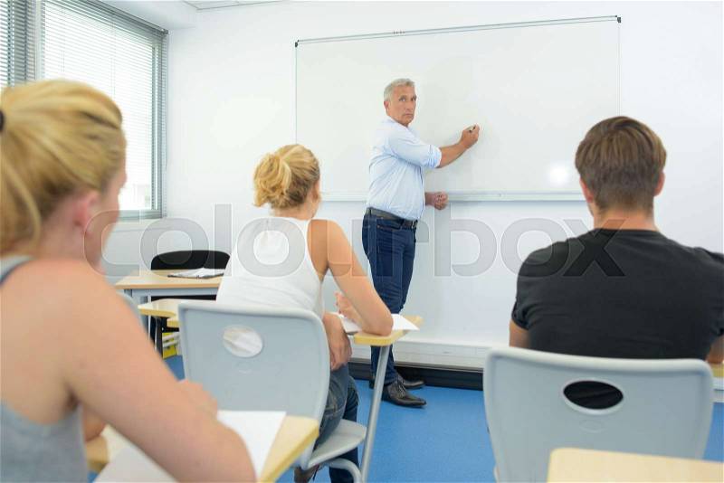 Teacher writing on white board in front of class, stock photo