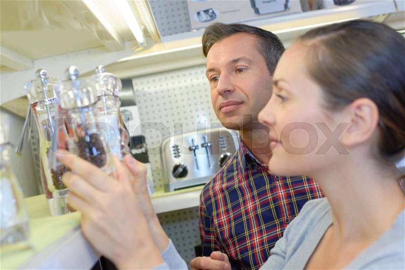 Couple choosing salt and pepper grinders in kitchenware shop, stock photo