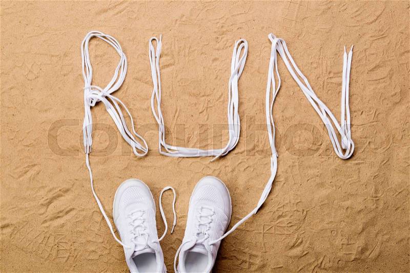 White running shoes and run sign made of shoelaces against sand background, studio shot, flat lay, stock photo