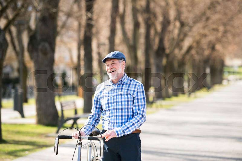 Handsome senior man in blue checked shirt with bicycle in town. Sunny spring day, stock photo