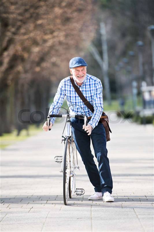 Handsome senior man in blue checked shirt with bicycle in town. Sunny spring day, stock photo