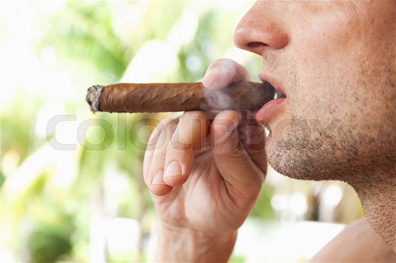Young European man smokes handmade cigar, close-up photo with selective focus. Dominican Republic, stock photo