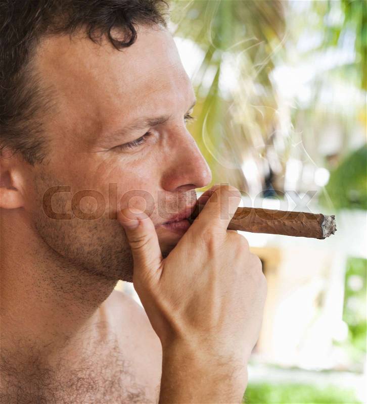 Young European man smokes big cigar, close up profile portrait with selective focus. Dominican Republic, stock photo