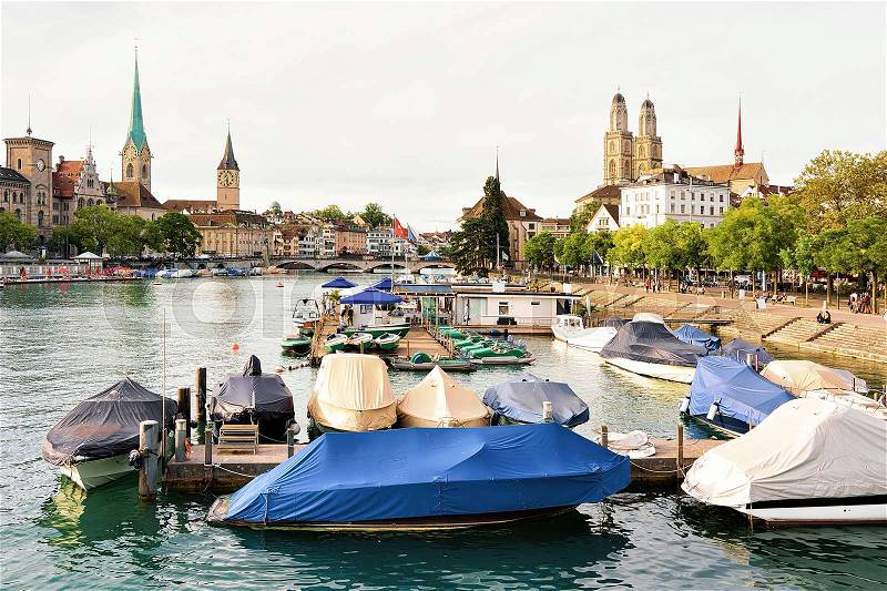 Grossmunster, St Peter Church and Fraumunster Church, and boats at Limmat River quay in the city center of Zurich, Switzerland. People on the background, stock photo
