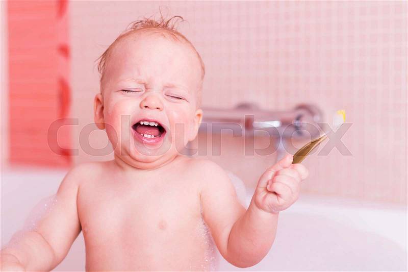 Crying baby boy getting teeth washed with toothbrush. Infant kid with a toothbrush in a tub, stock photo
