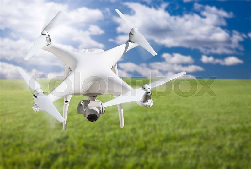 Unmanned Aircraft System (UAV) Quadcopter Drone In The Air Over Grass, stock photo