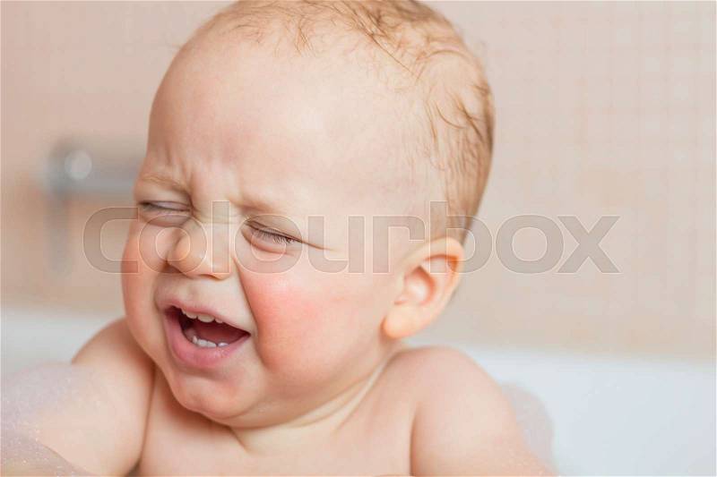Crying baby by in a bathtub. Infant kid sreaming while taking a bath, stock photo