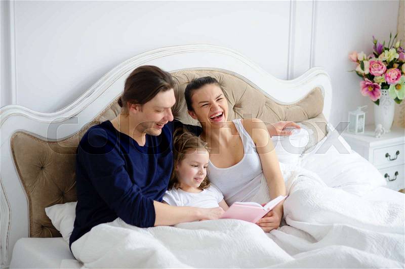 The little daughter reads to parents the book. Mother and the father cheerfully laugh. Morning of the day off in a young family, stock photo