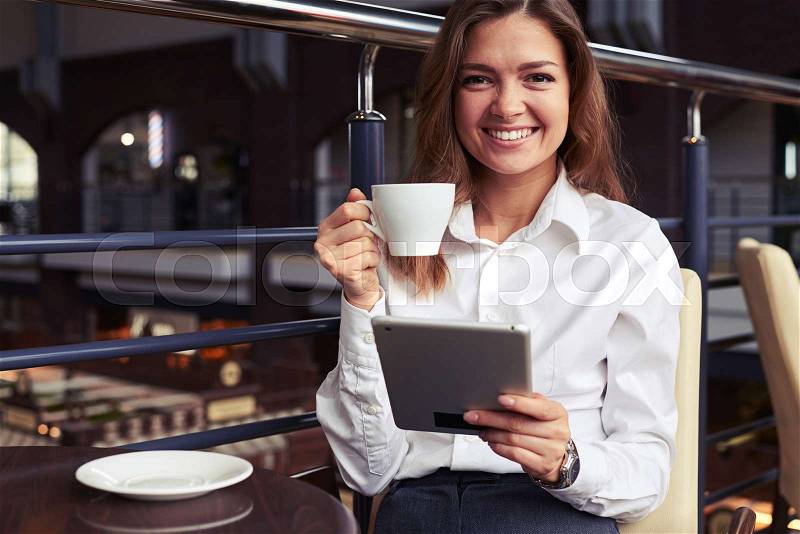 Close-up of laughing charming business woman enjoying tasty cup of coffee and reading latest news on tablet during break, stock photo