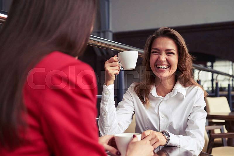 Over-the-Shoulder Shot of two beautiful laughing business women drinking coffee and enjoying nice conversation during lunch, stock photo