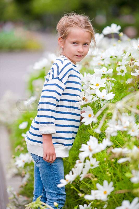 Little adorable girl smelling colorful flowers outdoors, stock photo