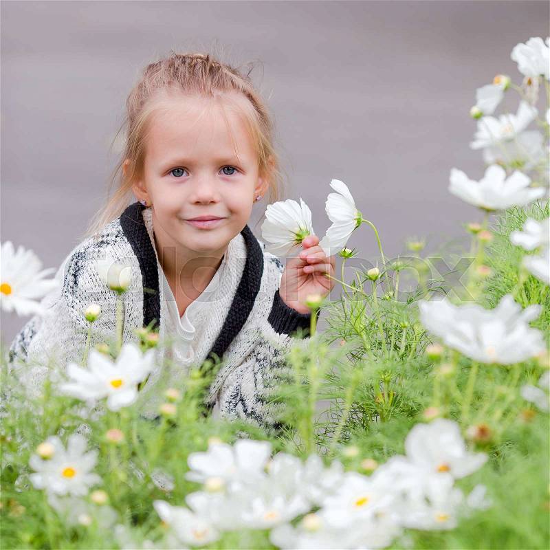 Little adorable girl smelling colorful flowers outdoors, stock photo