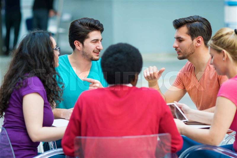 A group of teenagers sitting at the table in cafe, using laptop and drinking orange juice, stock photo