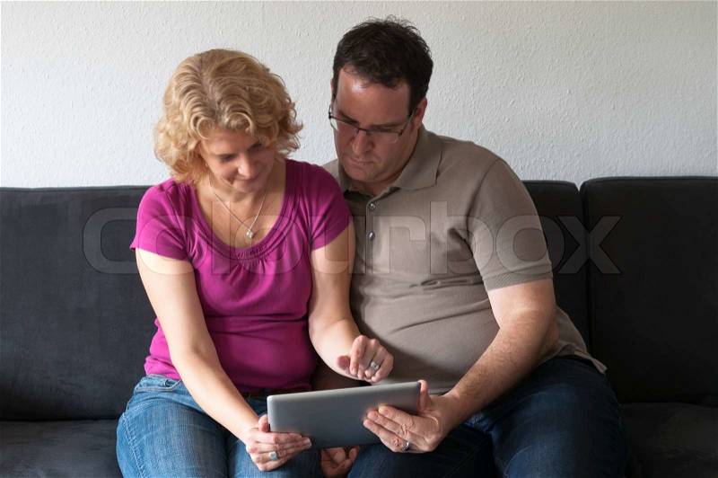Middle-aged couple sitting comfortably on a sofa and checking a digital tablet pc, stock photo