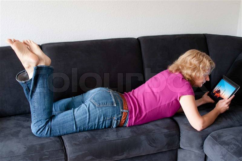 Middle-aged woman laying comfortably on a sofa and checking a digital tablet pc, stock photo