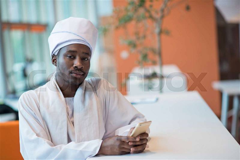 Sudanese business man in traditional outfit using mobile phone in office, stock photo