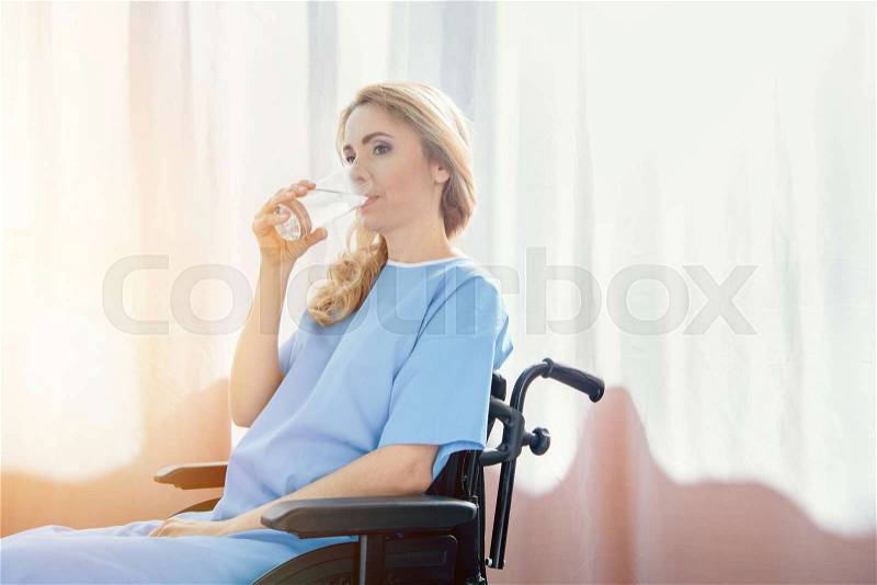 Side view of wheelchair woman drinking water in hospital, stock photo
