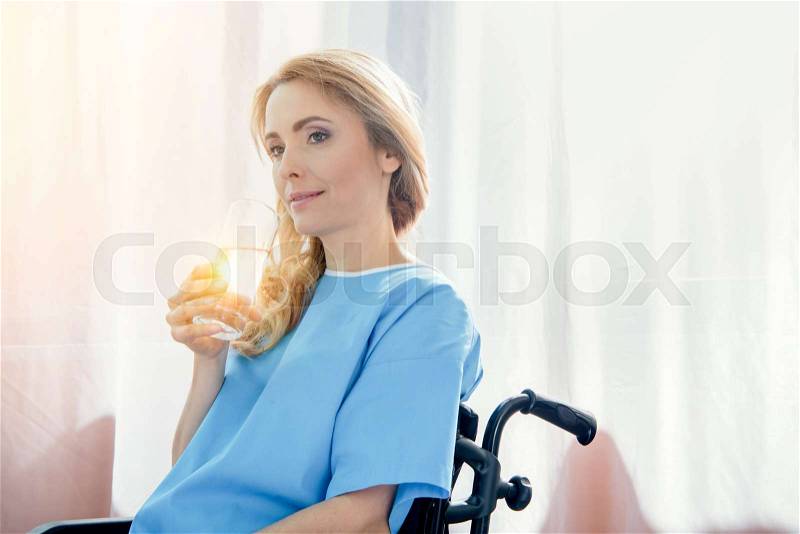 Side view of smiling wheelchair woman holding glass of water, stock photo