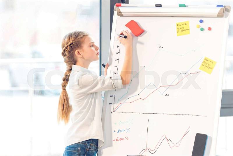 Little girl pretending to be businesswoman writing graphics on whiteboard in office, stock photo