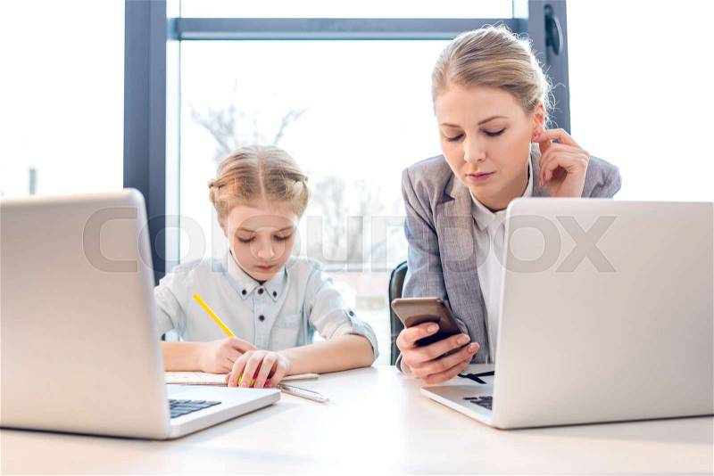 Mother and daughter talking while sitting at table with laptops in office, stock photo