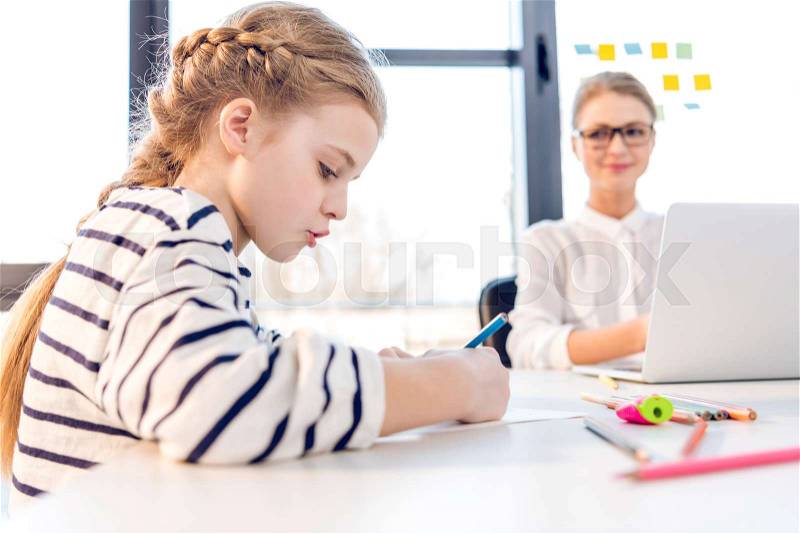Adorable daughter drawing, businesswoman working with laptop behind in office , stock photo