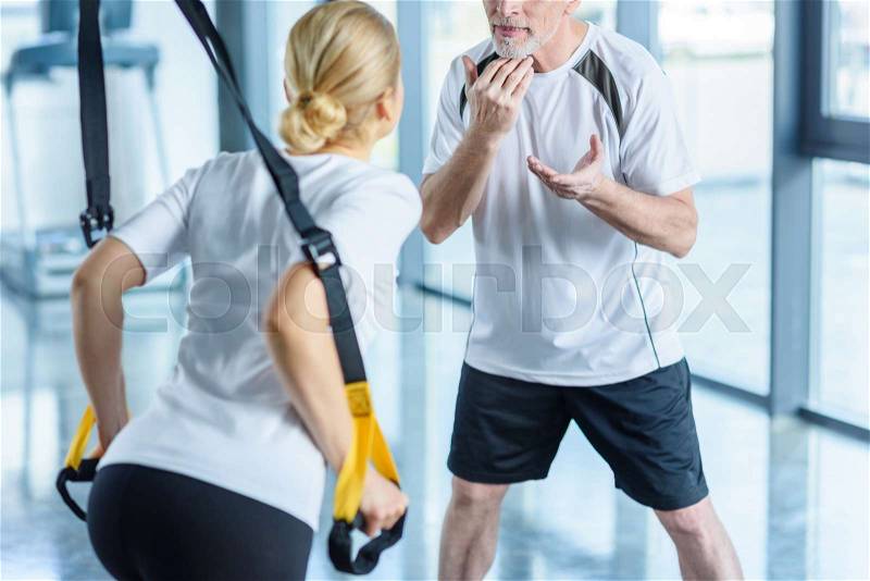 Sportswoman and senior trainer training with resistance band in sports center, stock photo