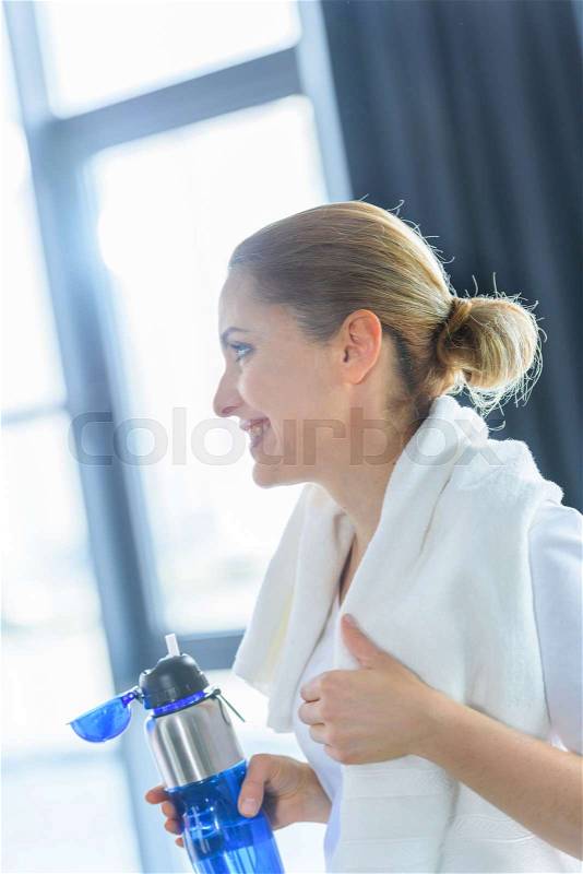 Sportswoman with towel holding sport bottle in sports center , stock photo