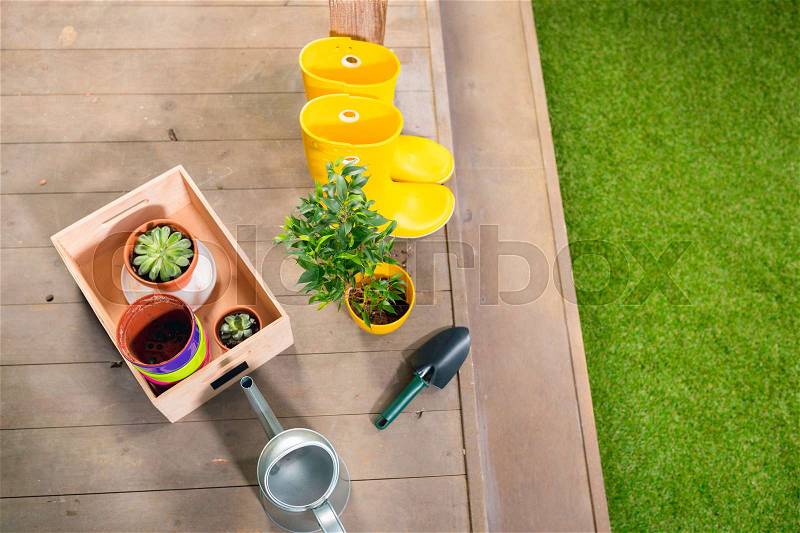 Watering can, yellow boots and plants in wooden box on porch, stock photo