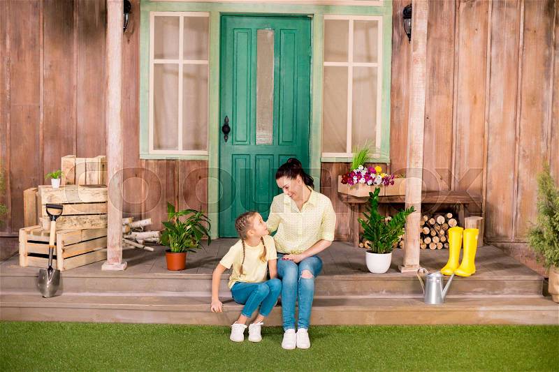 Happy mother and daughter sitting on porch and looking at each other, stock photo