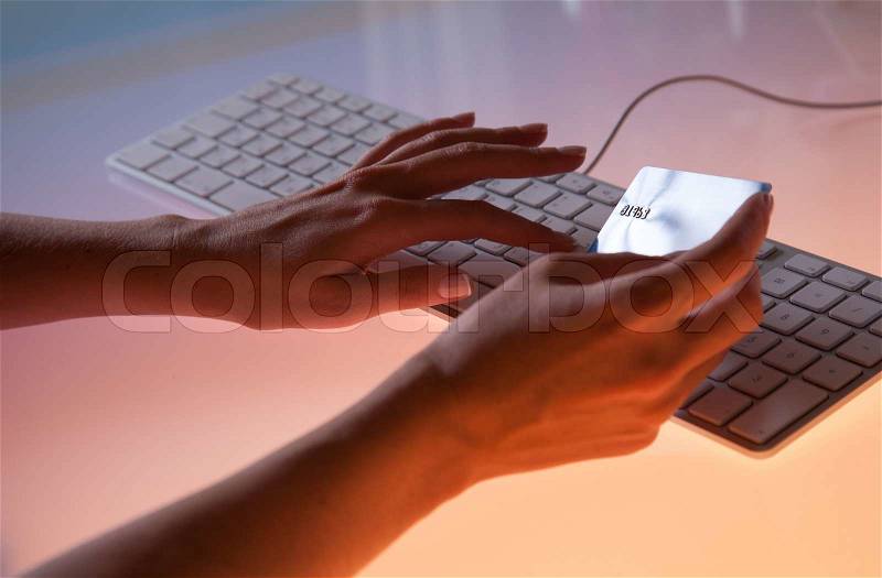 Woman\'s right hand holding a credit card above a keybord getting ready to enter data, stock photo