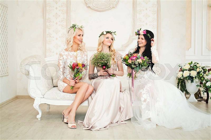 Beautiful Women in Evening Gown Sitting on the Sofa and Smiling. Perfect Hairstyle, Makeup and Flowers, stock photo