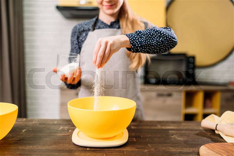 Female person adds sugar into a bowl, cake cooking on wooden table. Fresh tasty dough preparation, stock photo