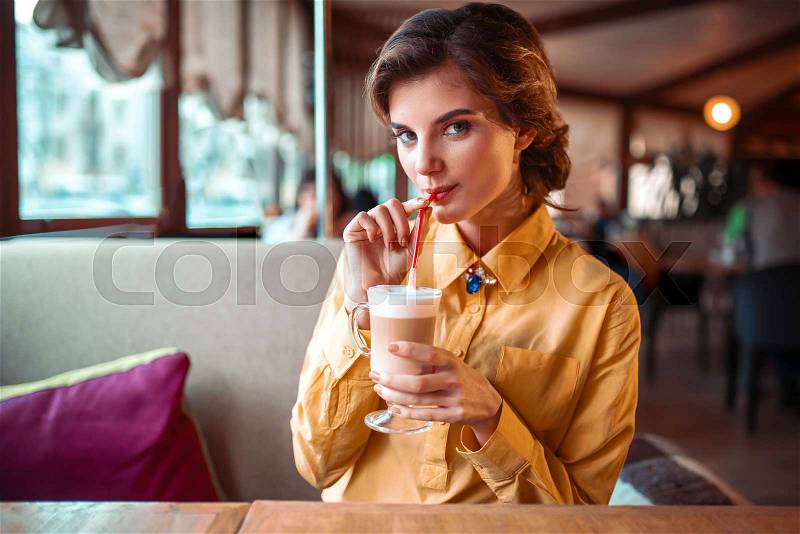 Attractive woman drinks a cocktail from the straw, restaurant on background, stock photo
