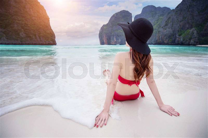 Young woman in red bikini sitting on the beach, stock photo