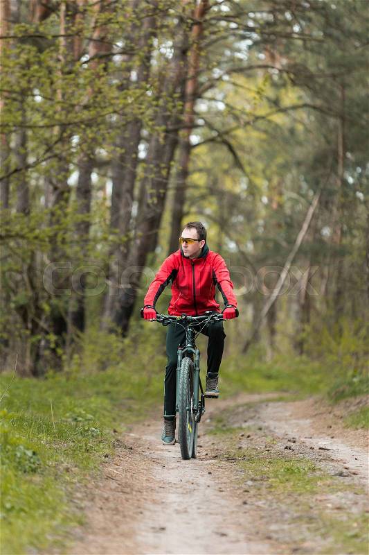 Young attractive man wears red suit ride the bike on the forest road, stock photo