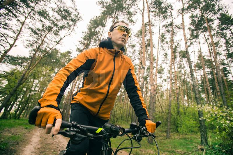 Young attractive man wears yellow suit ride the bike on the forest road, stock photo