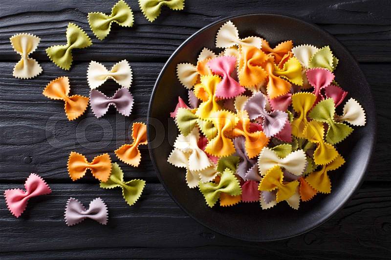 Beautiful Italian uncooked colored farfalle pasta close-up on a plate. horizontal view from above , stock photo