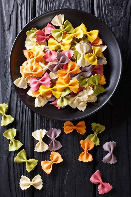 Beautiful Italian uncooked colored farfalle pasta close-up on a plate. Vertical view from above , stock photo
