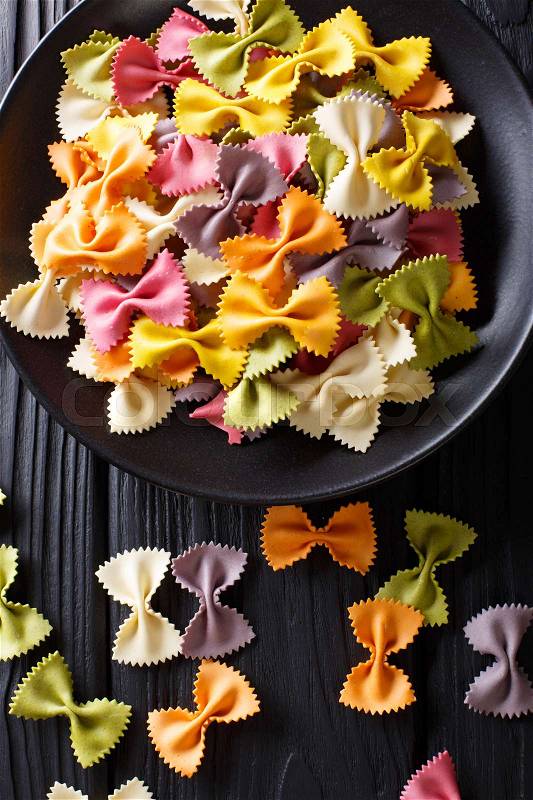 Italian natural colored farfalle pasta close-up on a plate on a black table. Vertical view from above , stock photo