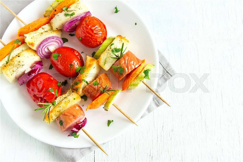 Grilled sausage and vegetables skewers with fresh herbs on white plate, stock photo