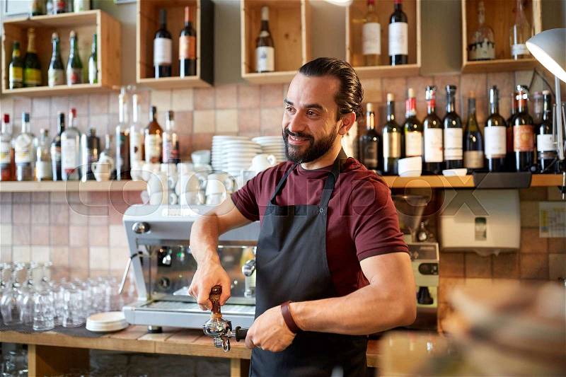 Small business, people and service concept - happy man or waiter in apron with holder and tamper preparing espresso at coffee shop, stock photo