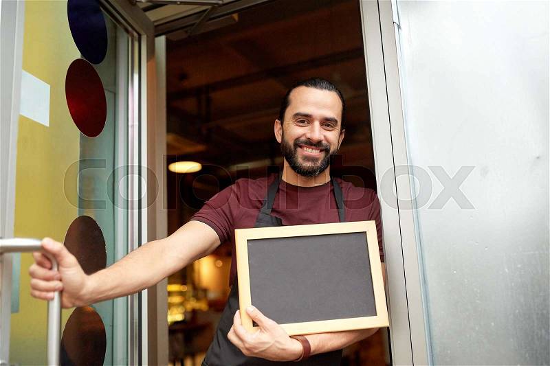 Small business, people and service concept - happy man or waiter with blackboard at bar or restaurant entrance door, stock photo