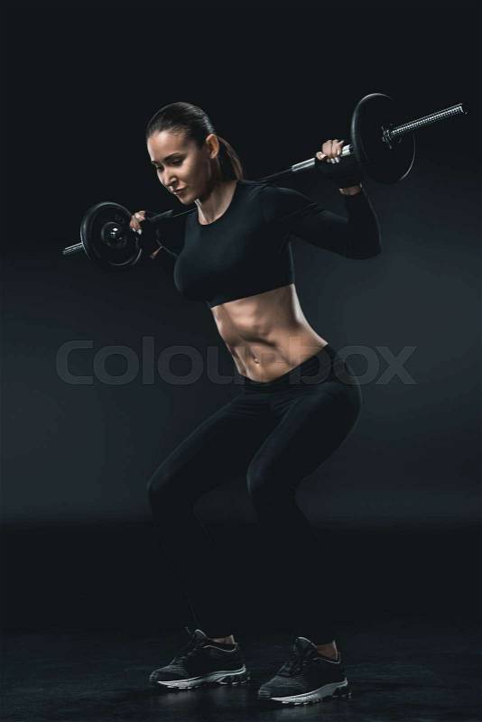 Young fitness woman squatting with barbell isolated on black. , stock photo
