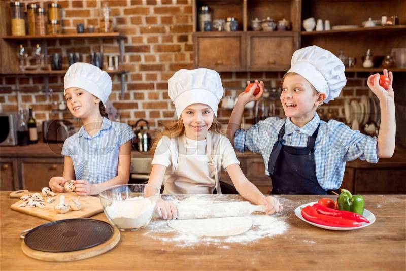 Children making pizza dough and preparing pizza ingredients in kitchen, stock photo