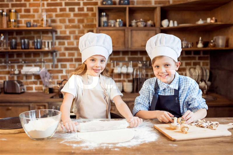 Children making pizza dough and preparing pizza ingredients in kitchen , stock photo